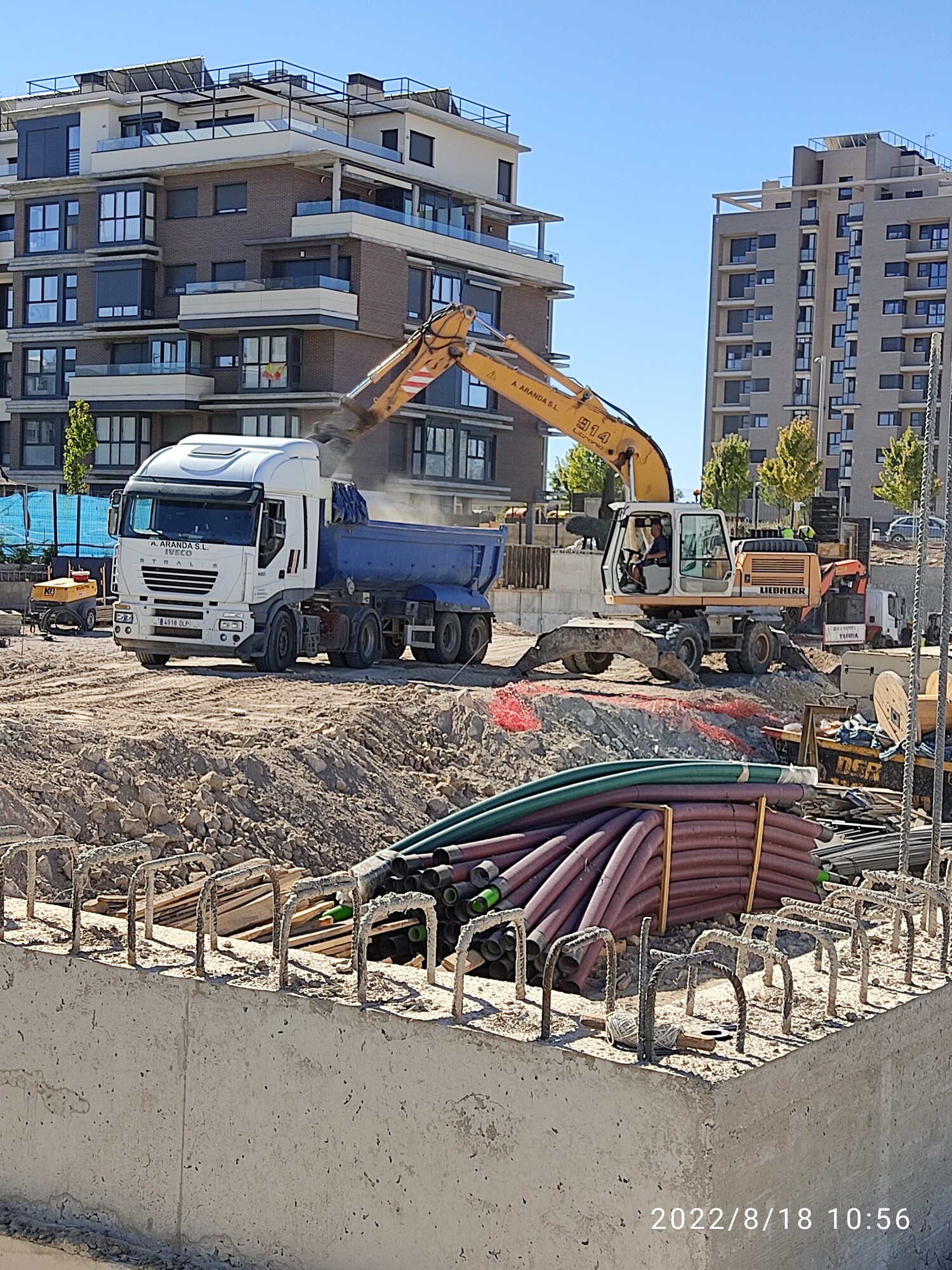 Excavadora cargando un camión en un sitio de construcción urbano.